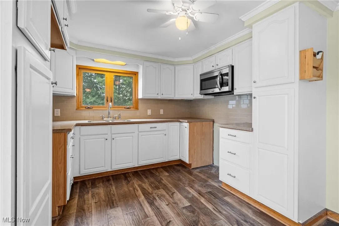 Kitchen with decorative backsplash, white cabinets, stainless steel microwave, dark wood-style flooring, and crown molding