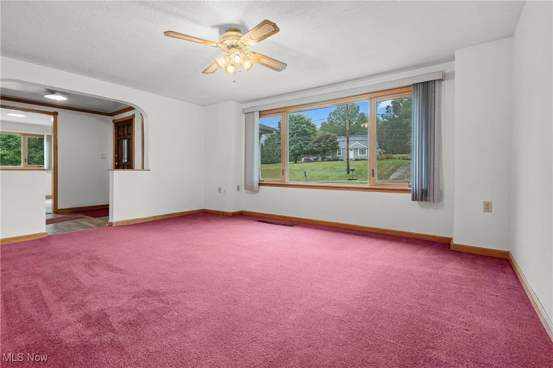 Carpeted empty room featuring plenty of natural light, arched walkways, a textured ceiling, and ceiling fan