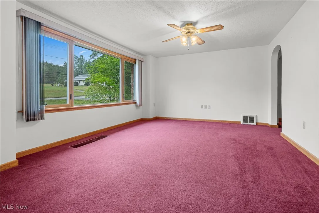 Unfurnished room featuring arched walkways, carpet, a textured ceiling, and a ceiling fan