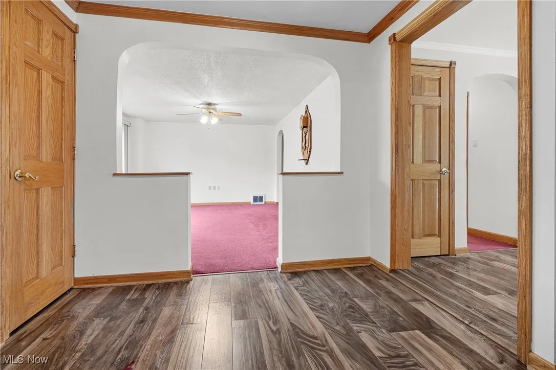 Empty room with arched walkways, dark wood-style flooring, ornamental molding, and a ceiling fan