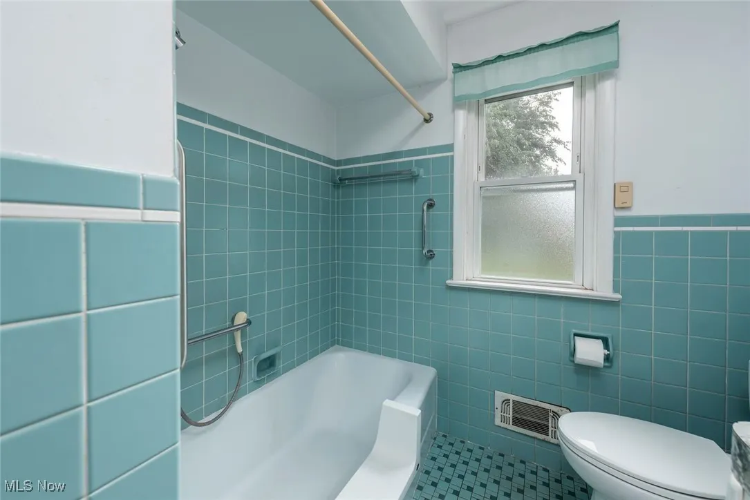 Bathroom featuring shower / washtub combination, tile walls, wainscoting, and tile patterned flooring