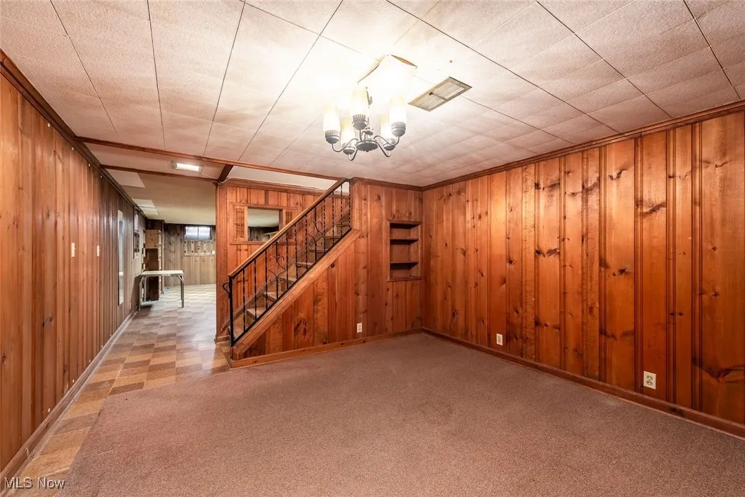 Basement featuring light flooring, wooden walls, stairway, and a chandelier