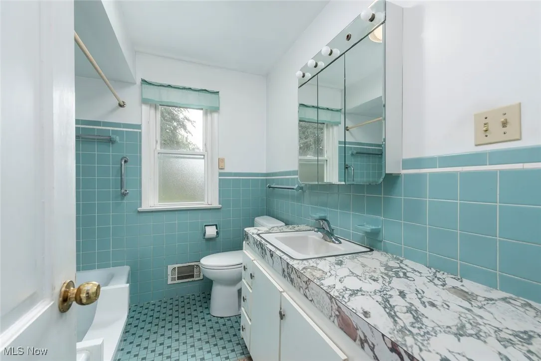 Full bath featuring tile walls, wainscoting, vanity, and shower / bath combo