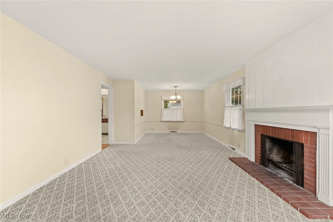 Unfurnished living room featuring carpet floors, a brick fireplace, and a chandelier