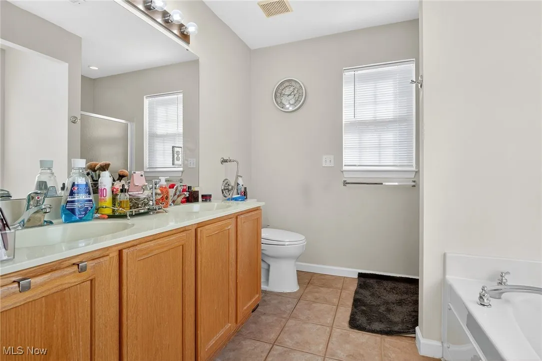 Bathroom with light tile patterned floors, a stall shower, double vanity, and a bath