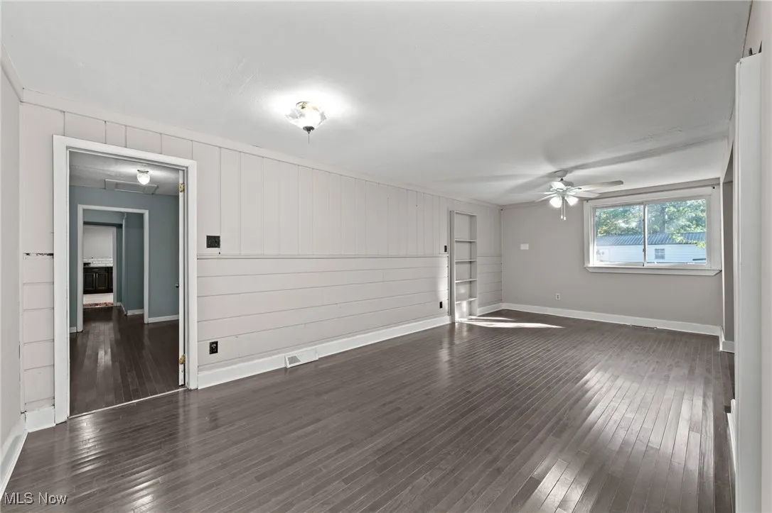 Unfurnished room with dark wood finished floors, a ceiling fan, and wood walls