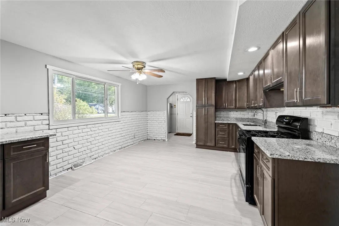 Kitchen featuring dark brown cabinetry, black gas range, arched walkways, light stone counters, and wainscoting