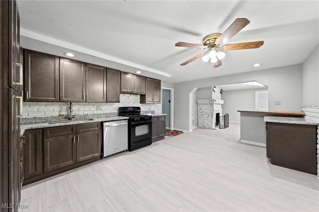 Kitchen with dark brown cabinets, black range with gas stovetop, arched walkways, recessed lighting, and dishwasher