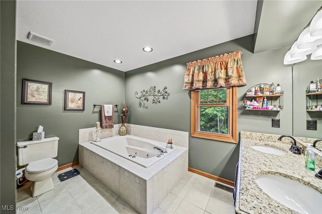 Bathroom featuring light tile patterned floors, a tub with jets, double vanity, and recessed lighting