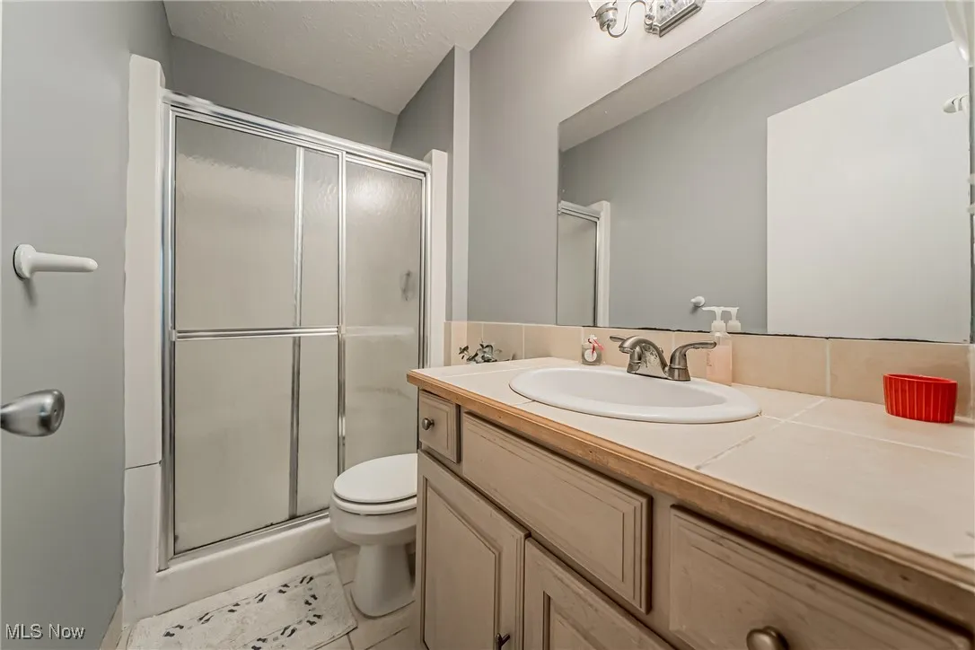 Full bathroom with vanity, a stall shower, a textured ceiling, and light tile patterned floors
