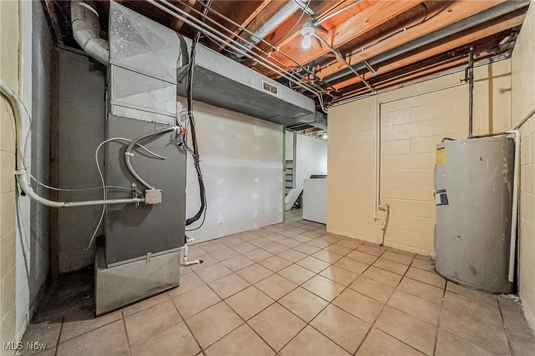 Unfinished basement with electric water heater, washer / clothes dryer, heating unit, and light tile patterned flooring