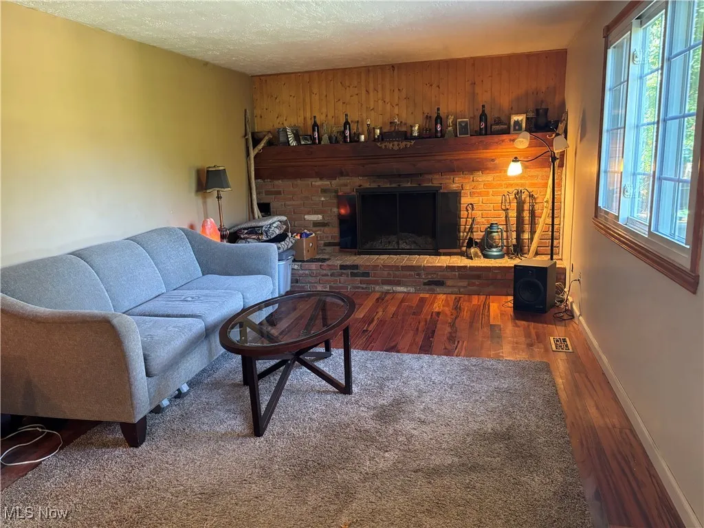 Living area featuring a brick fireplace, wood walls, wood finished floors, and a textured ceiling