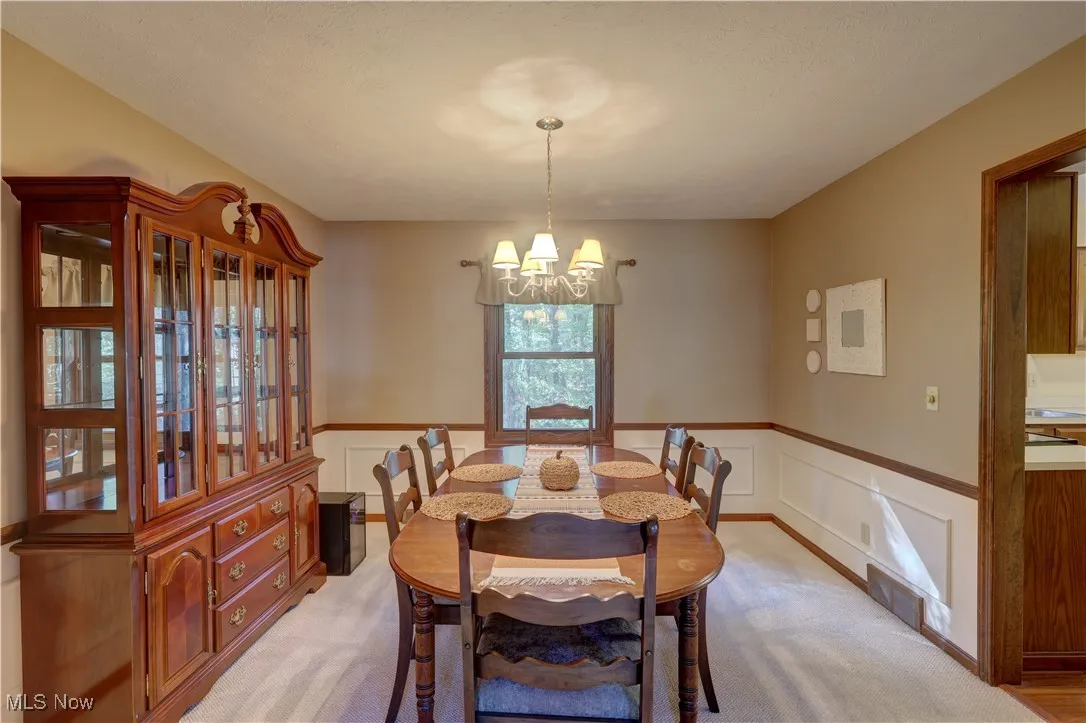 Dining room featuring wainscoting, light carpet, a decorative wall, and a chandelier