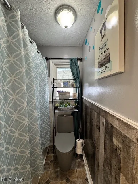 Bathroom with a textured ceiling, a wainscoted wall, a shower with curtain, wooden walls, and tile patterned flooring
