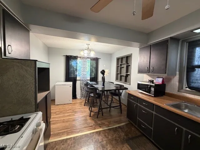 Kitchen featuring white gas range oven, dark wood finished floors, a chandelier, a ceiling fan, and decorative backsplash