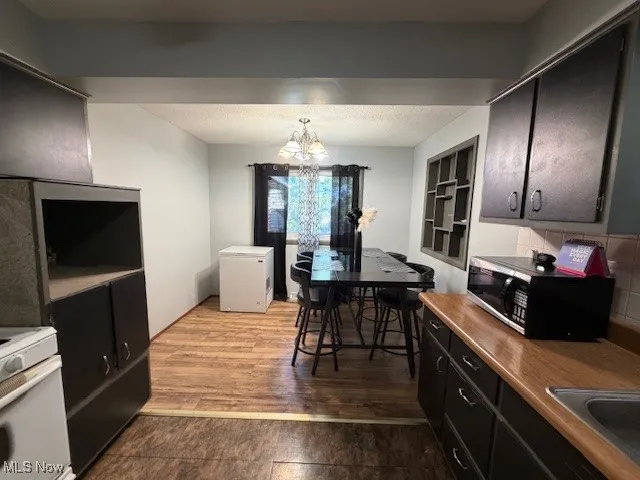 Kitchen with dark wood-style floors, a chandelier, white appliances, light countertops, and dark cabinets