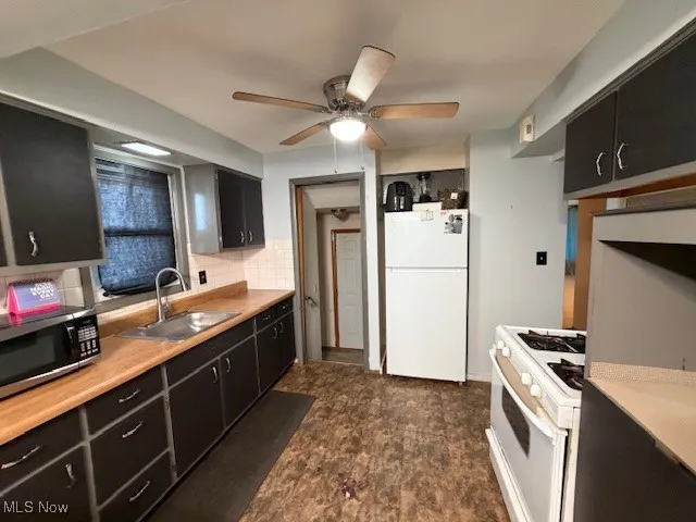 Kitchen with dark cabinetry, white appliances, light countertops, decorative backsplash, and a ceiling fan