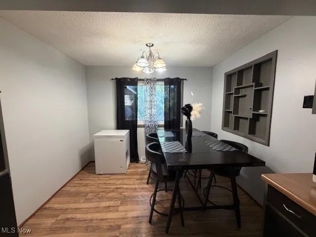 Dining space with a textured ceiling, a chandelier, and wood finished floors