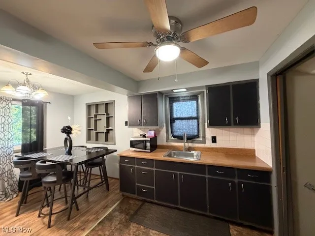 Kitchen with dark wood-style floors, light countertops, stainless steel microwave, ceiling fan, and decorative backsplash