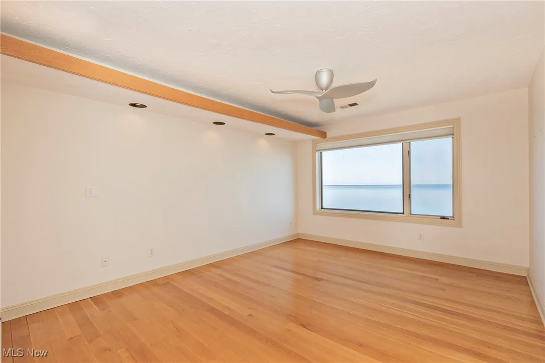 The primary bedroom features an oversized window and view of Lake Erie, recessed lighting and lovely hardwood flooring.