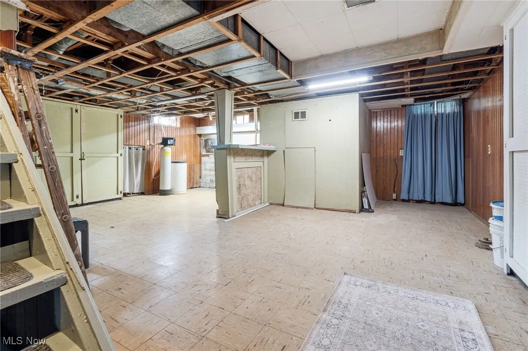 Basement with light floors, a water softener, and wooden walls
