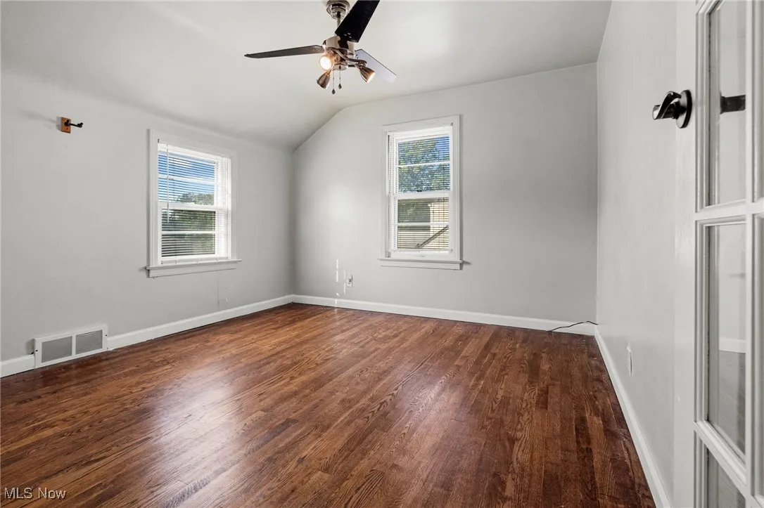 Unfurnished room featuring healthy amount of natural light, dark wood-type flooring, ceiling fan, and lofted ceiling
