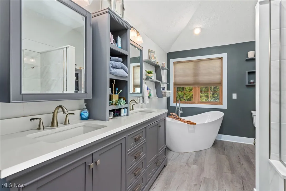 Bathroom with a freestanding bath, light wood-type flooring, double vanity, and lofted ceiling