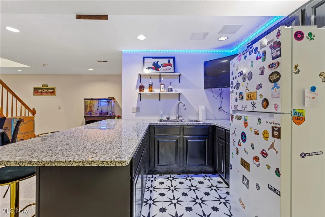 Kitchen featuring freestanding refrigerator, light stone countertops, a peninsula, open shelves, and recessed lighting