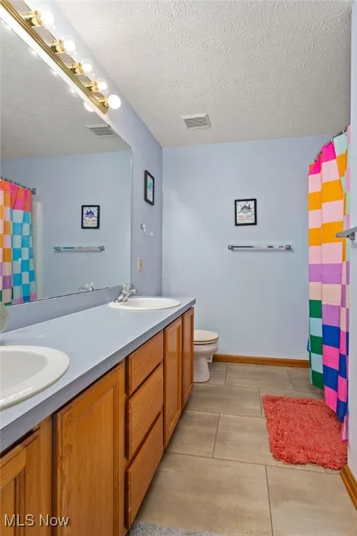 Bathroom with double vanity, a textured ceiling, and a shower with curtain