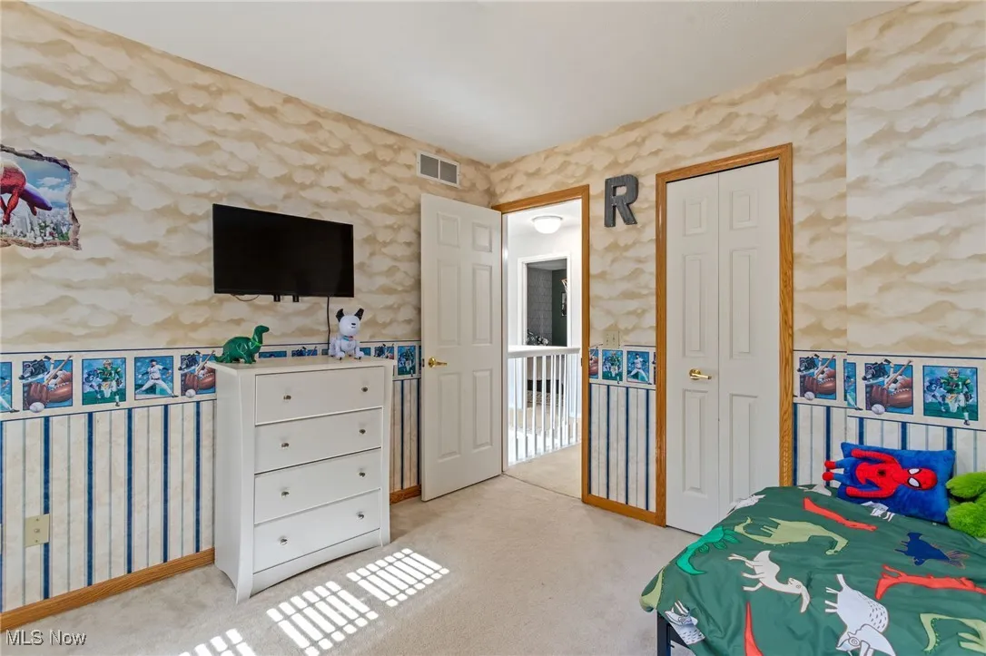 Bedroom featuring wallpapered walls, light colored carpet, and a closet