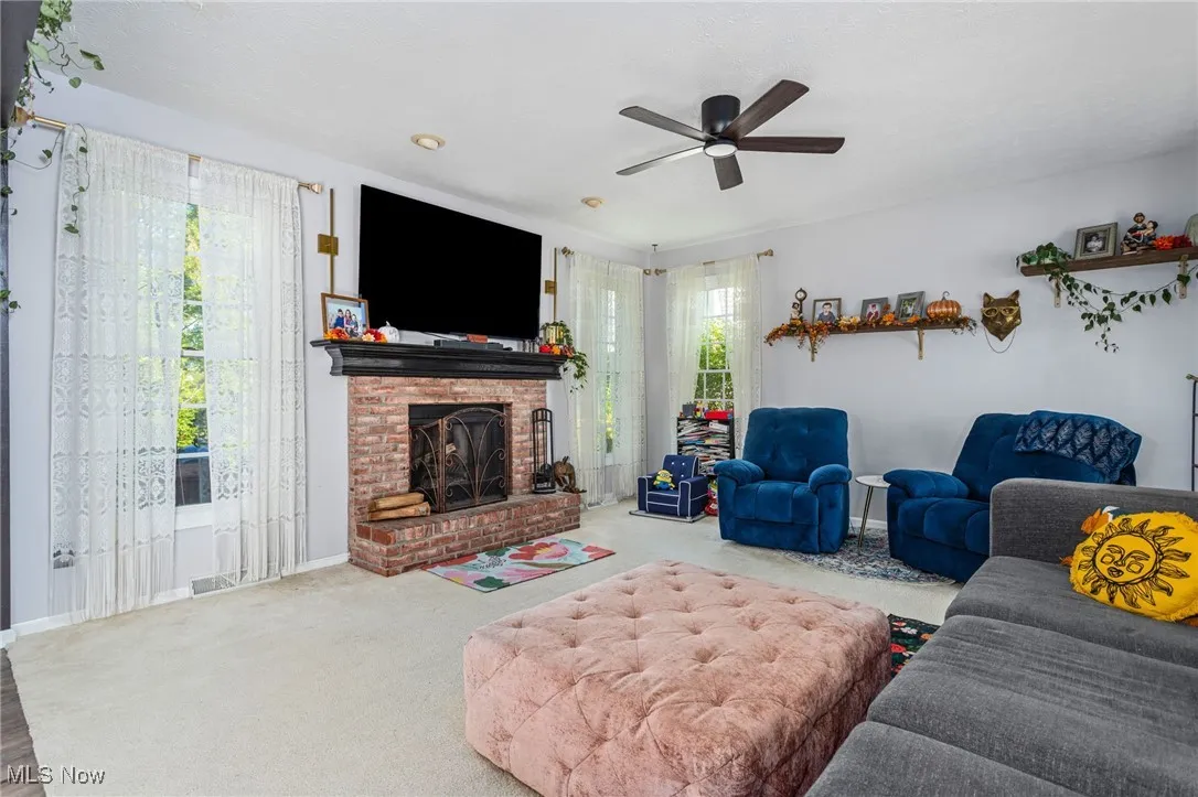Living area with carpet floors, a fireplace, and a ceiling fan
