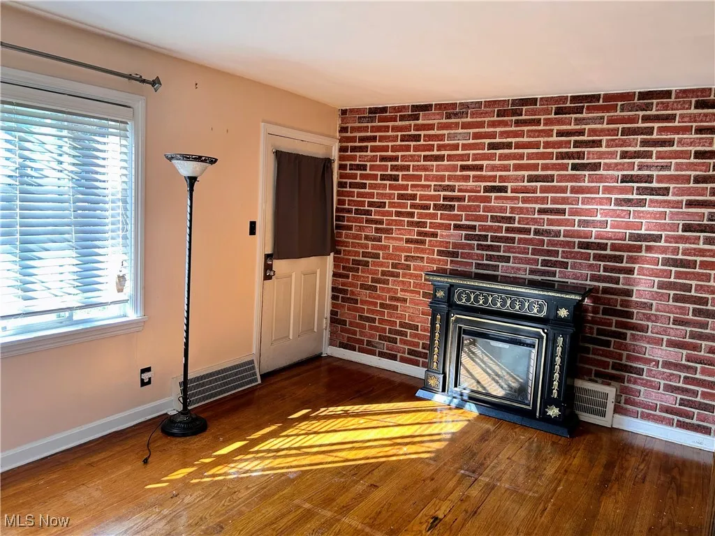 Unfurnished living room featuring dark wood-type flooring, brick wall, and a glass covered fireplace