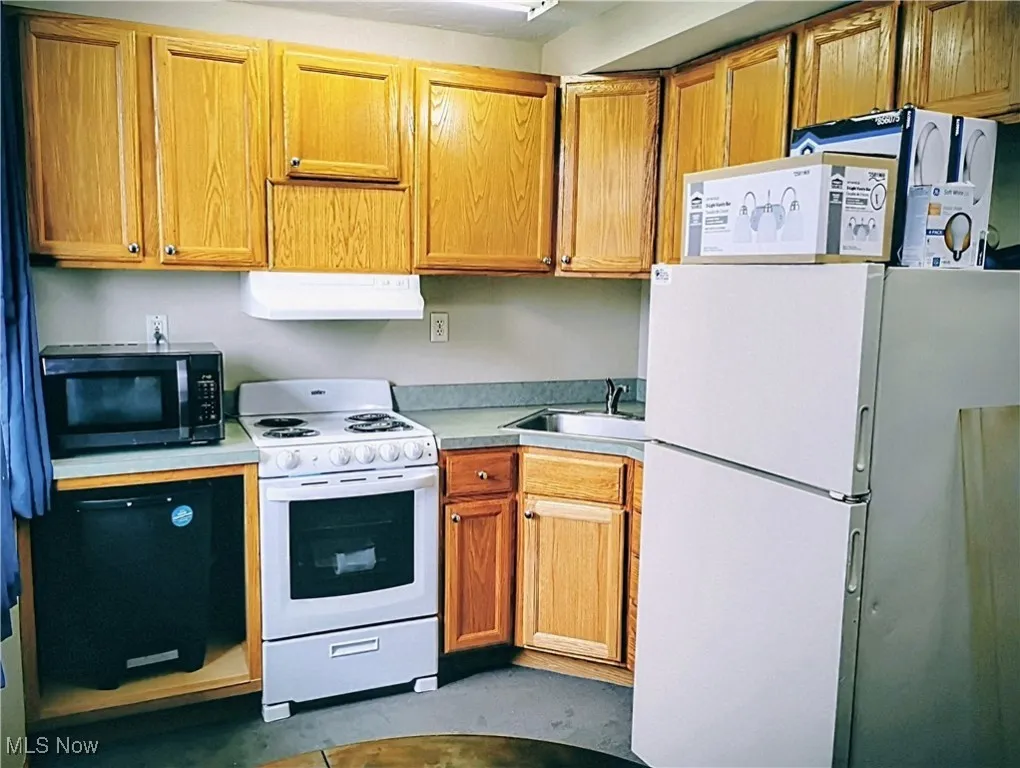 Kitchen with white appliances, light countertops, extractor fan, and brown cabinetry