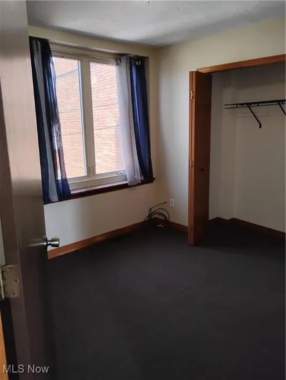 Unfurnished bedroom with dark carpet and a closet
