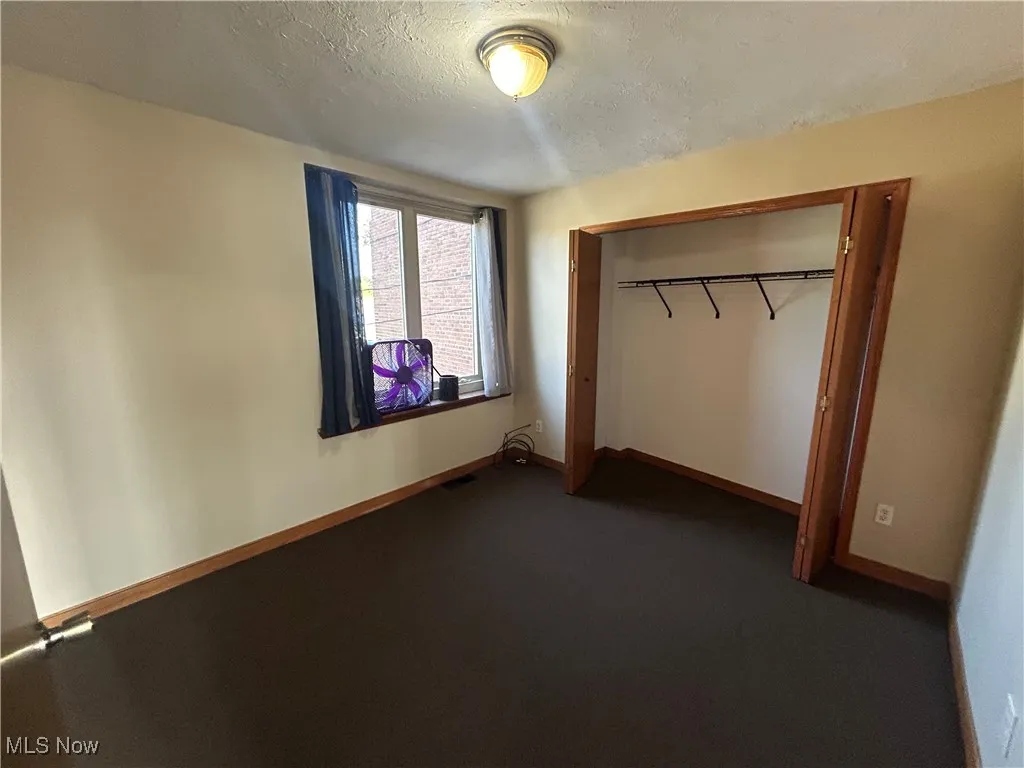 Unfurnished bedroom with a textured ceiling, a closet, and dark carpet