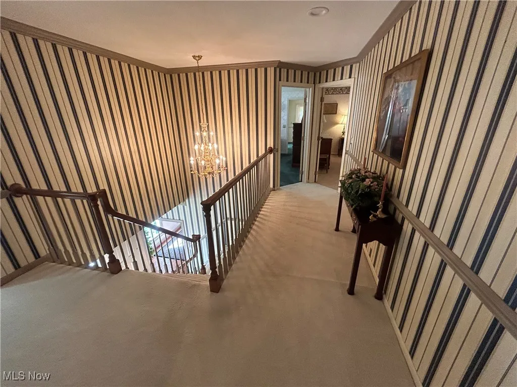 Hall featuring carpet flooring, wallpapered walls, an upstairs landing, a chandelier, and crown molding