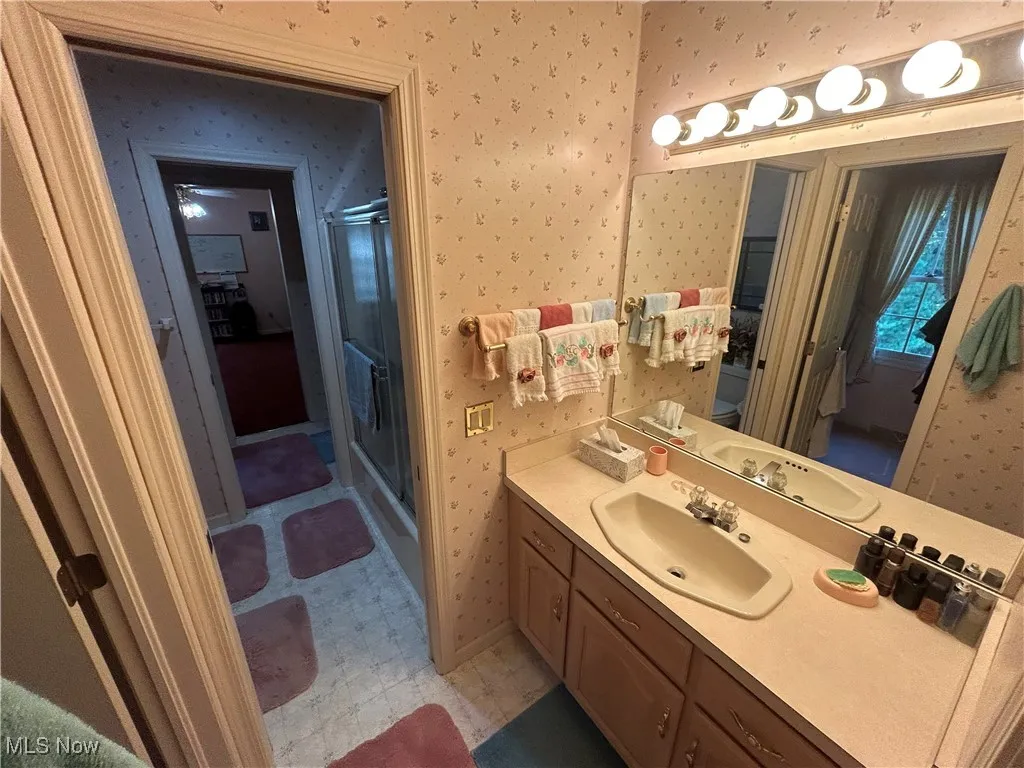 Full bathroom featuring wallpapered walls, vanity, a shower stall, and light flooring