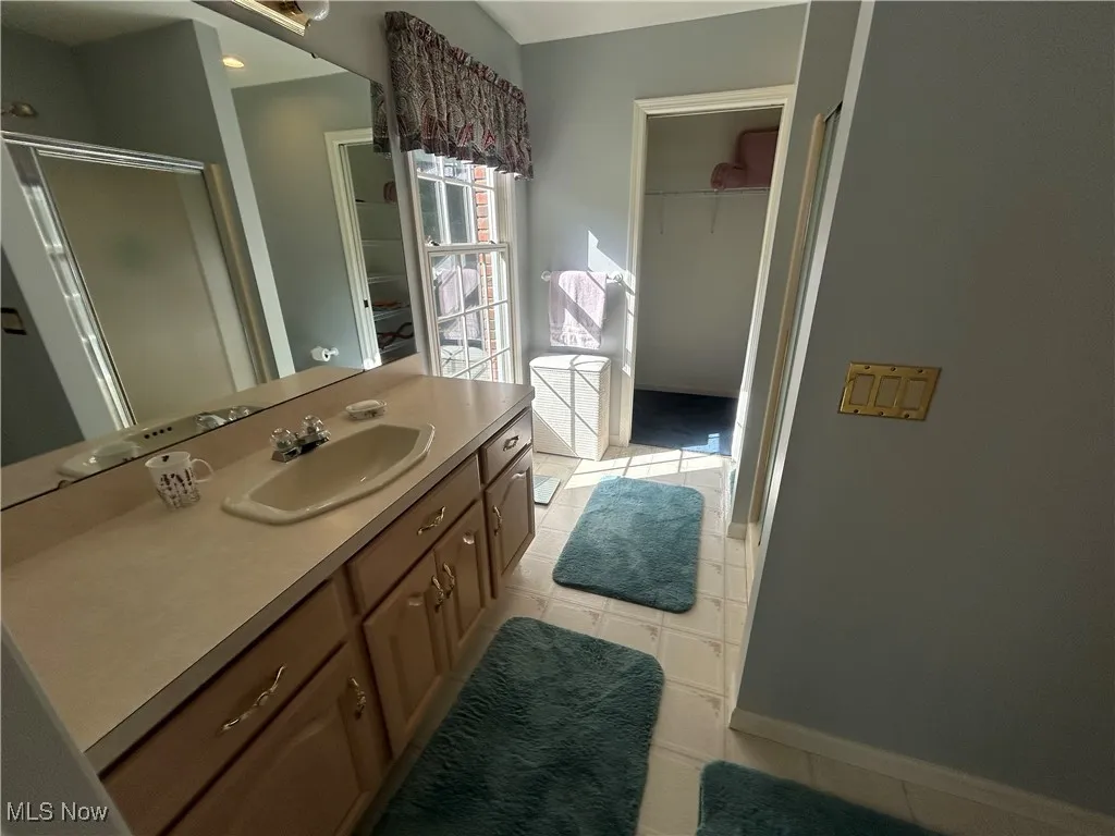 Bathroom featuring a shower stall, vanity, light tile patterned flooring, and a spacious closet