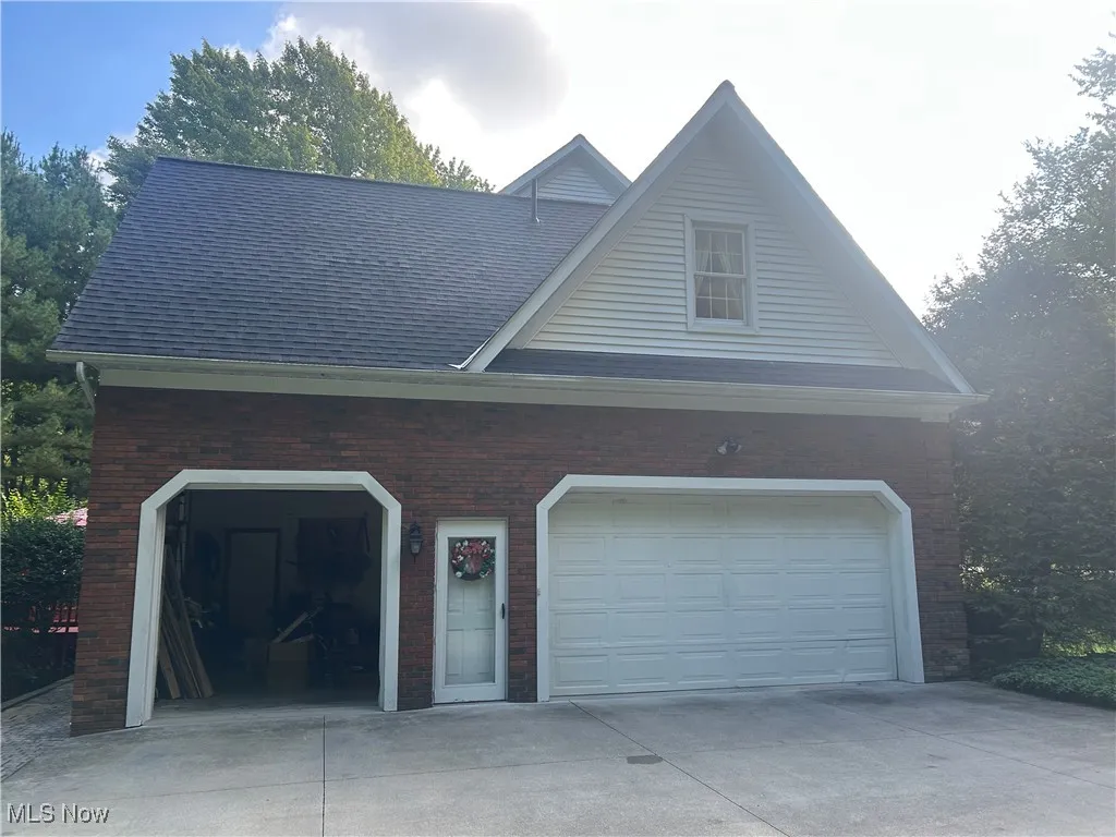 View of side of property featuring concrete driveway, a garage, a shingled roof, and brick siding