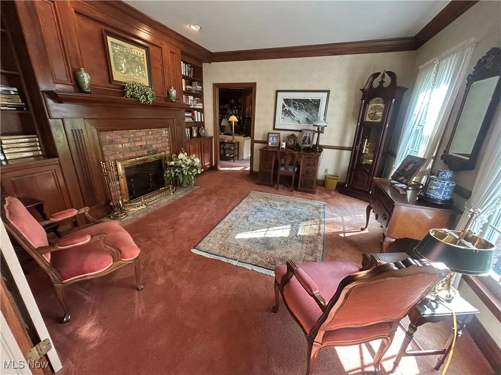 Library featuring a brick fireplace, ornamental molding, and wallpapered walls
