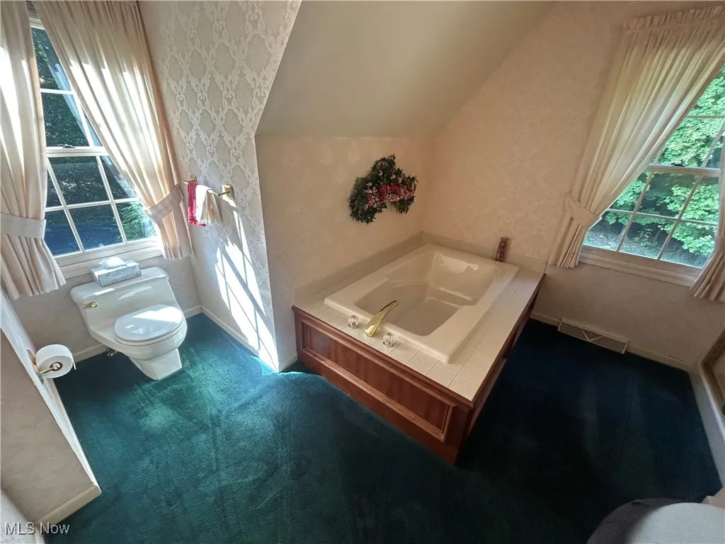 Bathroom with wallpapered walls, a garden tub, and lofted ceiling