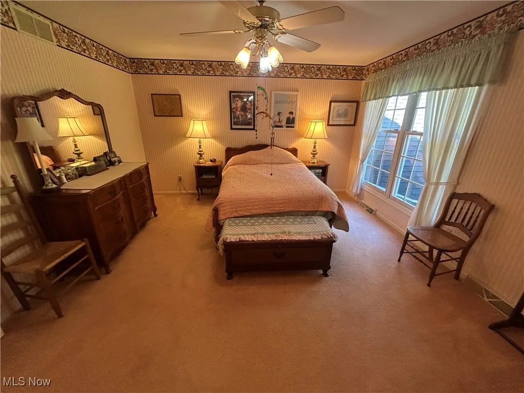 Bedroom with light colored carpet, a ceiling fan, and wallpapered walls