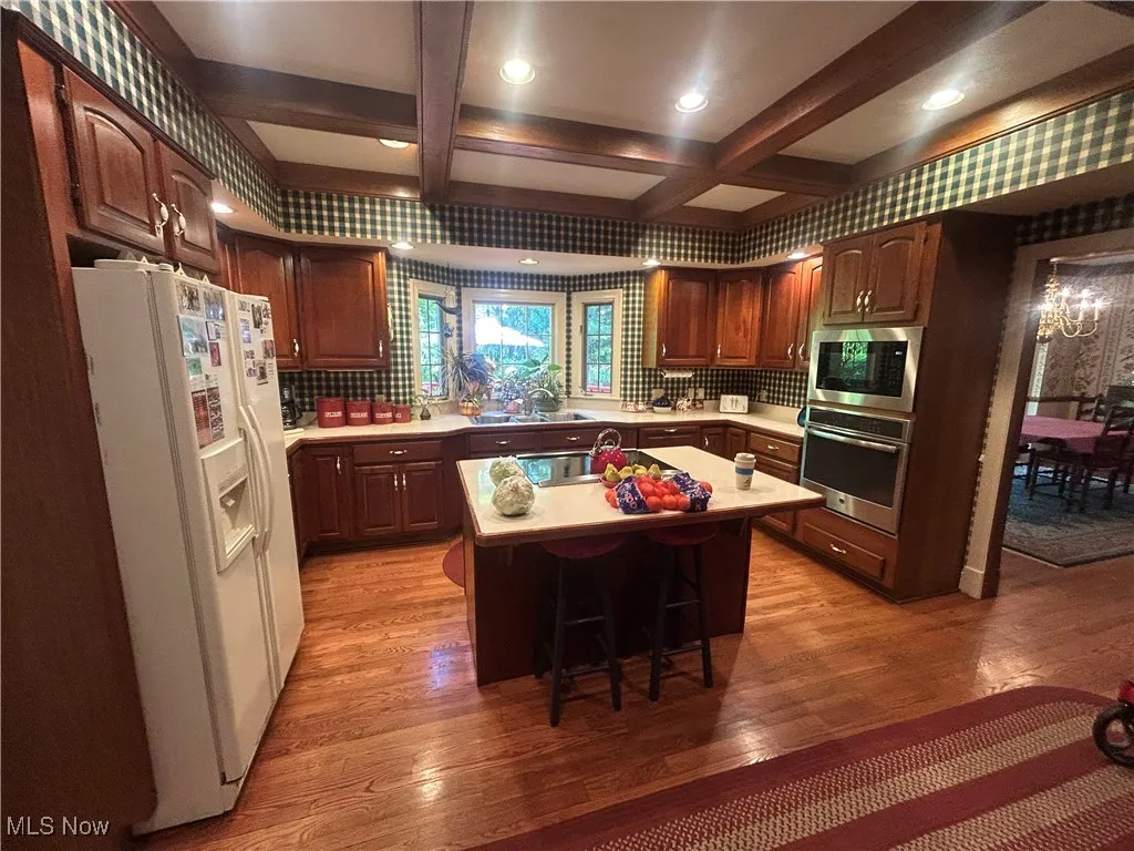 Kitchen with appliances with stainless steel finishes, light countertops, light wood-type flooring, a breakfast bar area, and beam ceiling