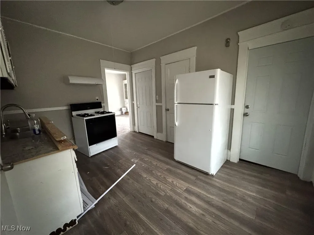 Kitchen with white appliances, dark wood-style floors, white cabinetry, and range hood