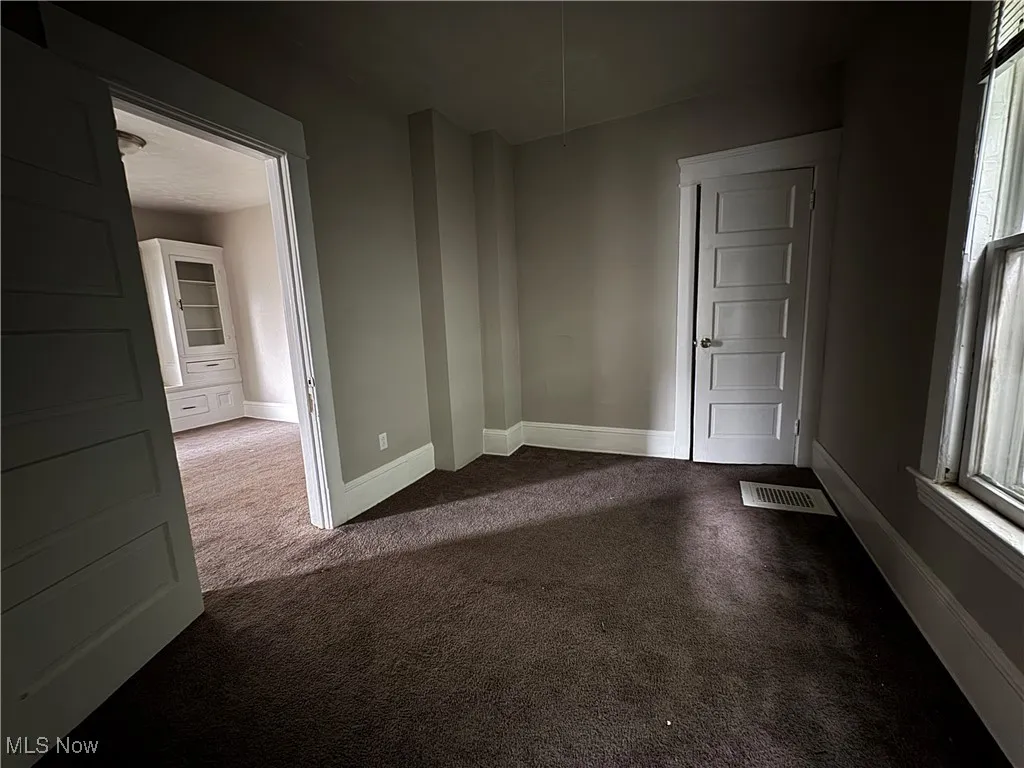 Spare room featuring dark carpet and baseboards