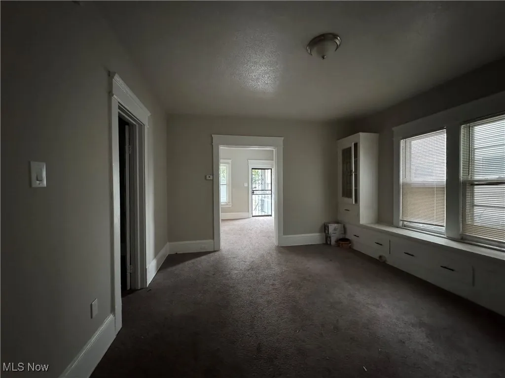 Unfurnished room featuring dark carpet and baseboards