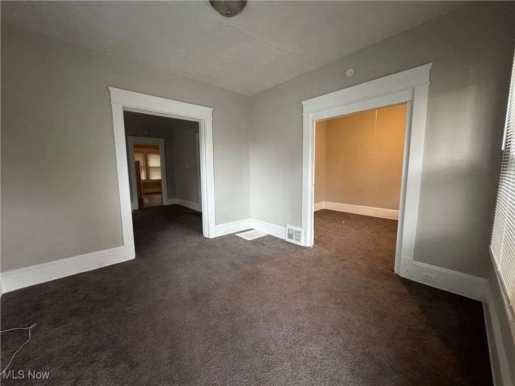 Unfurnished room featuring dark colored carpet and baseboards