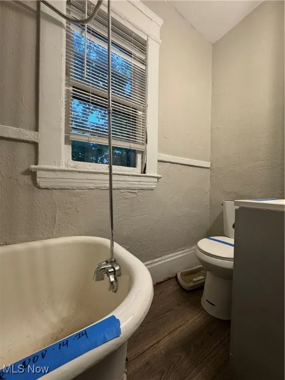 Full bath featuring a textured wall, a freestanding bath, and dark wood-style flooring