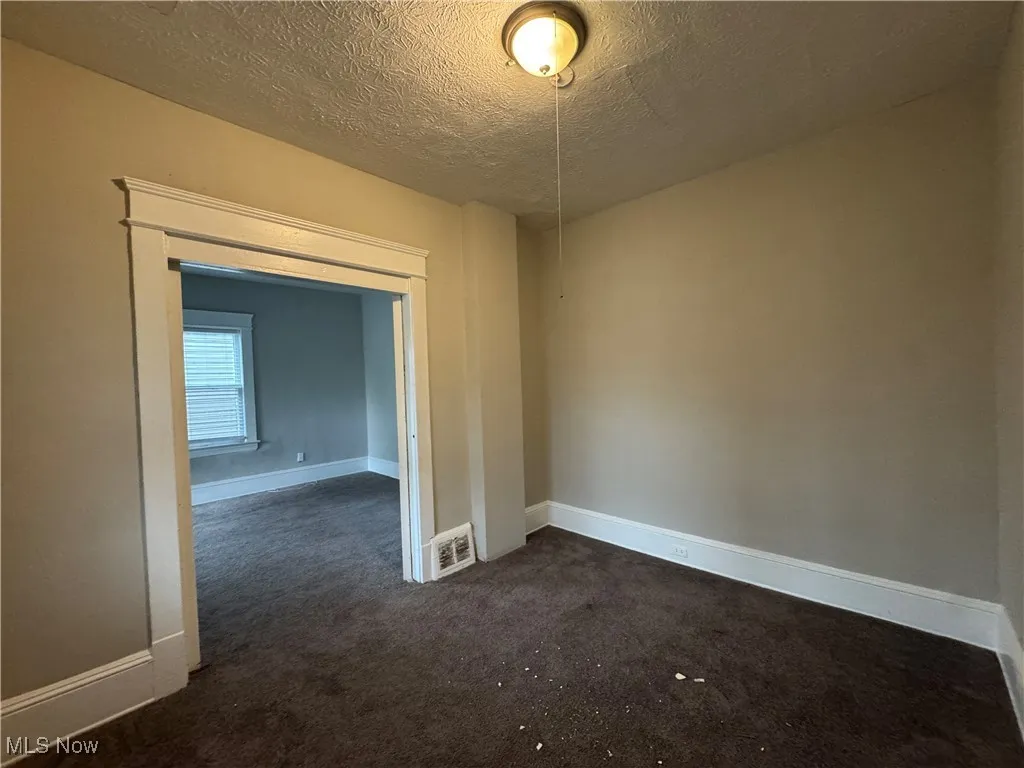 Empty room featuring dark colored carpet and a textured ceiling