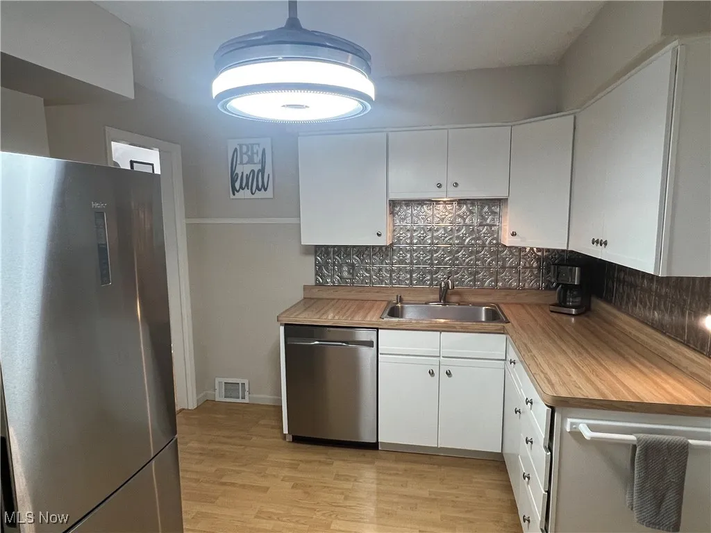Kitchen featuring appliances with stainless steel finishes, decorative backsplash, white cabinets, light wood finished floors, and light countertops